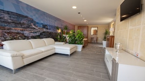 A modern living room with a white sofa, a stone wall mural, and a kitchen area with a TV mounted above the counter. - 39 St. George (Victoria)