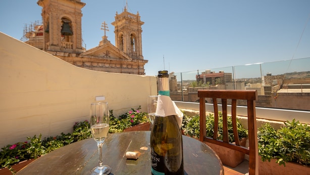 A bottle of wine, a glass, and a chair on a table with a view of a historic building in the background. - 39 St. George (Victoria)