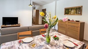 Zona pranzo con tavolo apparecchiato per due, televisore sullo sfondo e un mobile con un quadro sopra.