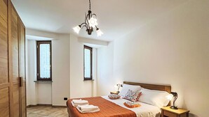 Una camera da letto con un letto, due comodini, una lampada da notte, un lampadario e due finestre.