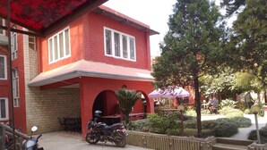 Un edificio de ladrillo rojo con un patio cubierto, una motocicleta estacionada al frente y un pequeño jardín con escalones que conducen a la entrada.