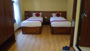 Habitación de hotel con dos camas, cabeceros de madera, un armario de madera y una pequeña alfombra en el suelo.
