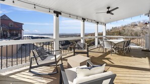 A covered outdoor deck with seating, a table, and a view of a house and landscape.