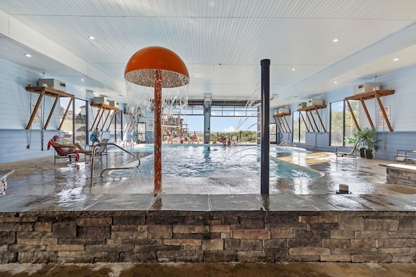 An indoor swimming pool with a stone wall in the foreground, a large orange water feature, and multiple air conditioning units mounted on the walls.