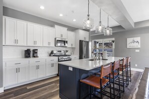 A modern kitchen with white cabinets, a large island with bar stools, stainless steel appliances, and pendant lighting.