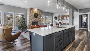 A modern kitchen with a large island, a brick accent wall, and a fireplace.