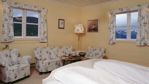 A room with a bed, two floral-patterned sofas, a table with a lamp, and two windows with curtains. - Fossli Hotel (Eidfjord)