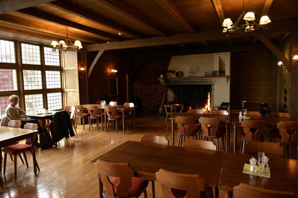 Un vaste espace dédié à la salle à manger, avec des tables et des chaises en bois, une cheminée et de grandes fenêtres laissant entrer la lumière naturelle.
