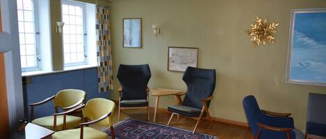 A room with a wooden floor, two windows, a patterned rug, and four chairs.