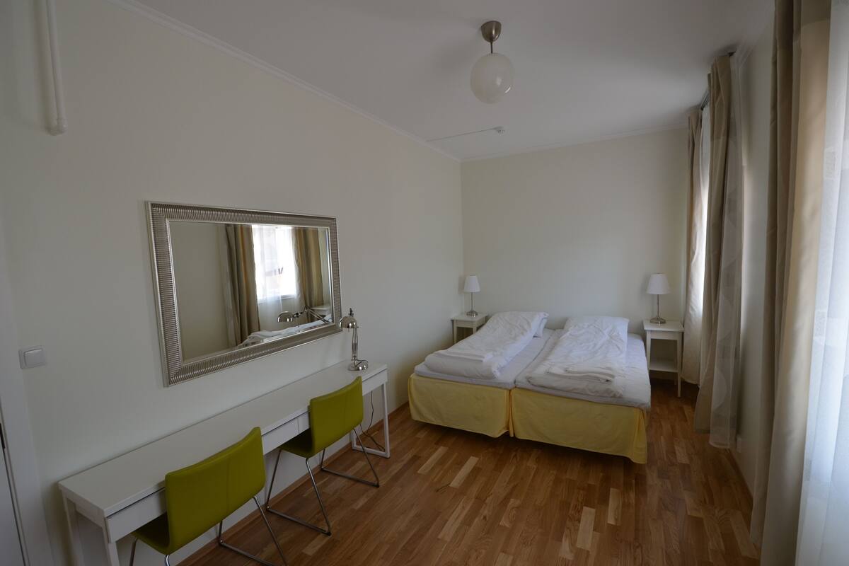 A hotel room with a bed, a desk, a chair, a mirror, and a ceiling light.