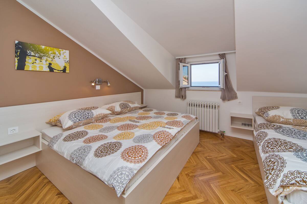 A bedroom with two beds, a radiator, a window with curtains, and a wall-mounted light fixture.