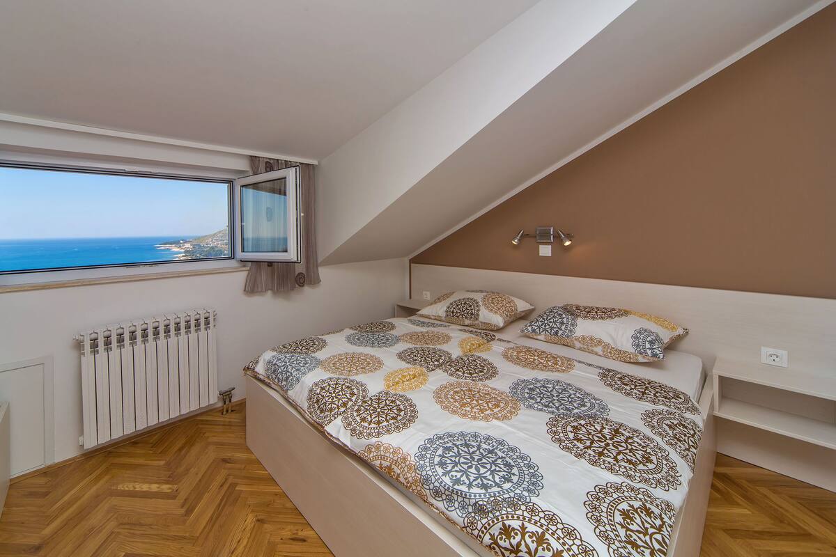 A bedroom with a large bed, a view of the sea, a radiator, and a ceiling light.