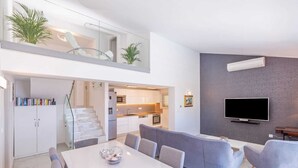 A modern apartment with a dining area, grey sofa, TV, and a kitchen in the background. - Villa Laura (Zupa dubrovacka)