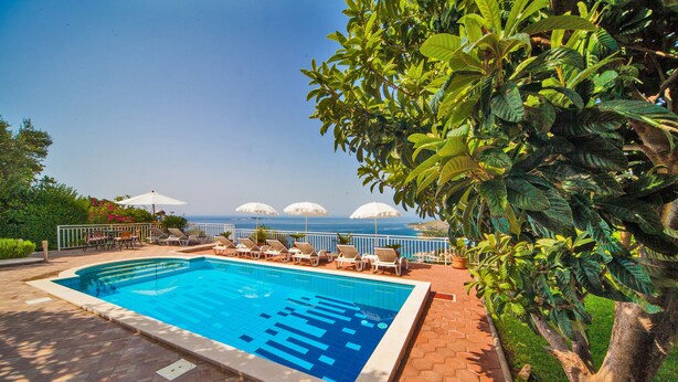A swimming pool with lounge chairs and umbrellas, surrounded by greenery and a view of the sea. - Villa Laura (Zupa dubrovacka)