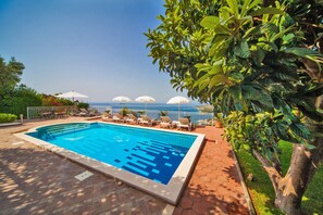 A swimming pool with lounge chairs and umbrellas, surrounded by greenery and a view of the sea. - Villa Laura (Zupa dubrovacka)