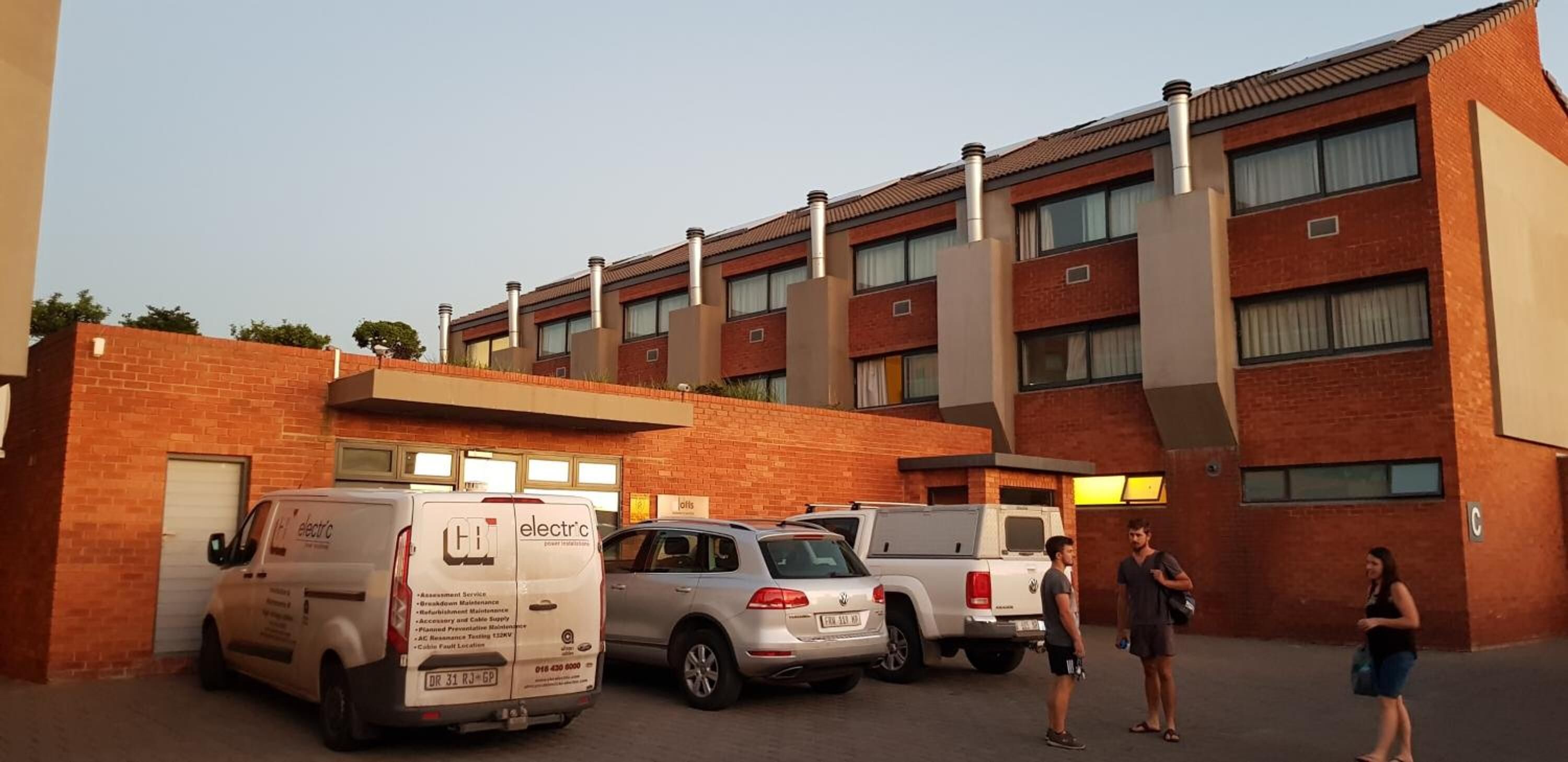 A building with multiple floors, a brick facade, and several parked vehicles, including a van and a car.
