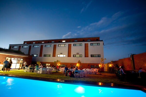 A modern building with multiple windows and a flat roof, surrounded by a swimming pool and outdoor seating areas.