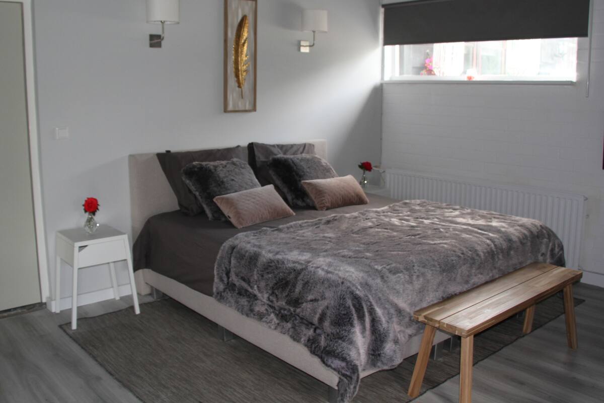 A bedroom with a bed, bedside tables, a bench, a window, and a radiator.