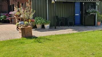A covered outdoor seating area with chairs and tables, surrounded by potted plants and a brick pathway.
