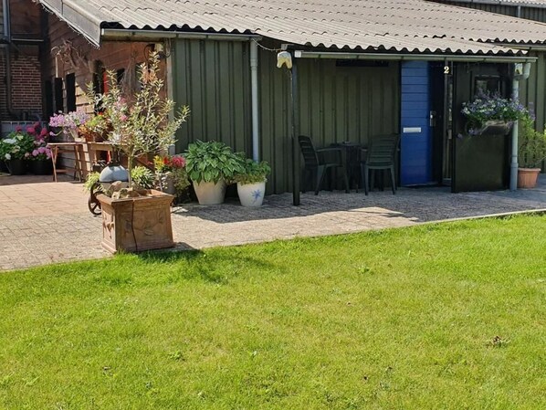 A covered outdoor seating area with chairs and tables, surrounded by potted plants and a brick pathway. - B&B De Rekkendonken (Liempde)