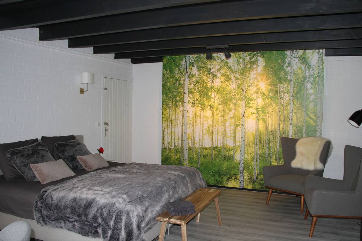 A bedroom with a bed, a chair, a bench, and a wall mural of a forest.