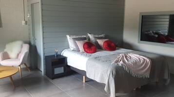 Una camera da letto con un letto, una sedia, un comodino, un tavolino e una TV a parete.