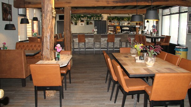 Un restaurante con mesas y sillas de madera, una zona de bar y lámparas colgantes.
