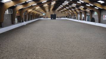 Una arena interior con suelo de arena, vigas de madera y varias puertas.