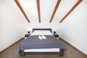 A modern bedroom with a large bed, wooden beams on the ceiling, and a nightstand with a lamp. - Marojica Apartments (Konavle)