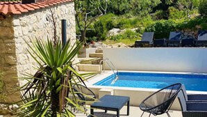 A poolside area with a stone wall, a potted plant, lounge chairs, and a swimming pool. - Marojica Apartments (Konavle)