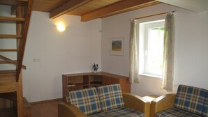 A cozy living room with a wooden staircase, two plaid sofas, a small wooden table, and a window with curtains.