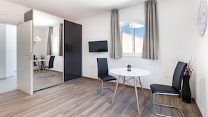 Une chambre moderne avec un plancher en bois, une table ronde, deux chaises, un téléviseur et une grande fenêtre avec des rideaux.