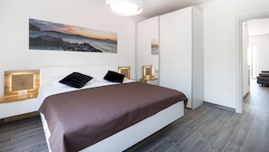 Une chambre à coucher moderne avec un grand lit, un tableau représentant un coucher de soleil, des lampes de chevet et une armoire.