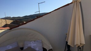 A bed with a headboard, pillows, and a blanket in a room with a sloped ceiling and a view of buildings and hills. - Casa Karuza (Pag)
