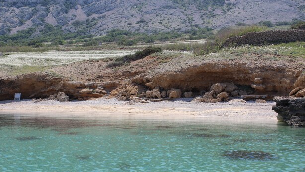 A coastal landscape with clear turquoise water, rocky terrain, and sparse vegetation. - Casa Karuza (Pag)