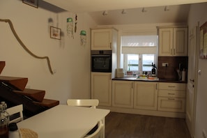 A compact kitchen with a built-in oven, a dining area with a white table and chairs, and a window providing natural light. - Casa Karuza (Pag)