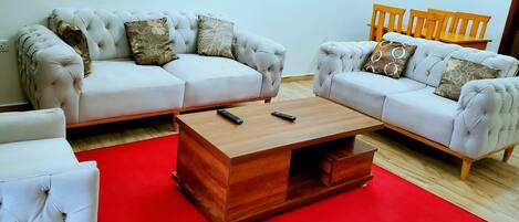 Uma sala de estar com dois sofás brancos, uma mesa de centro de madeira e um tapete vermelho.