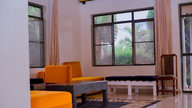 A room with large windows, a sofa, a bench, and a chair. - Green View Apart Hotel (Kigali)