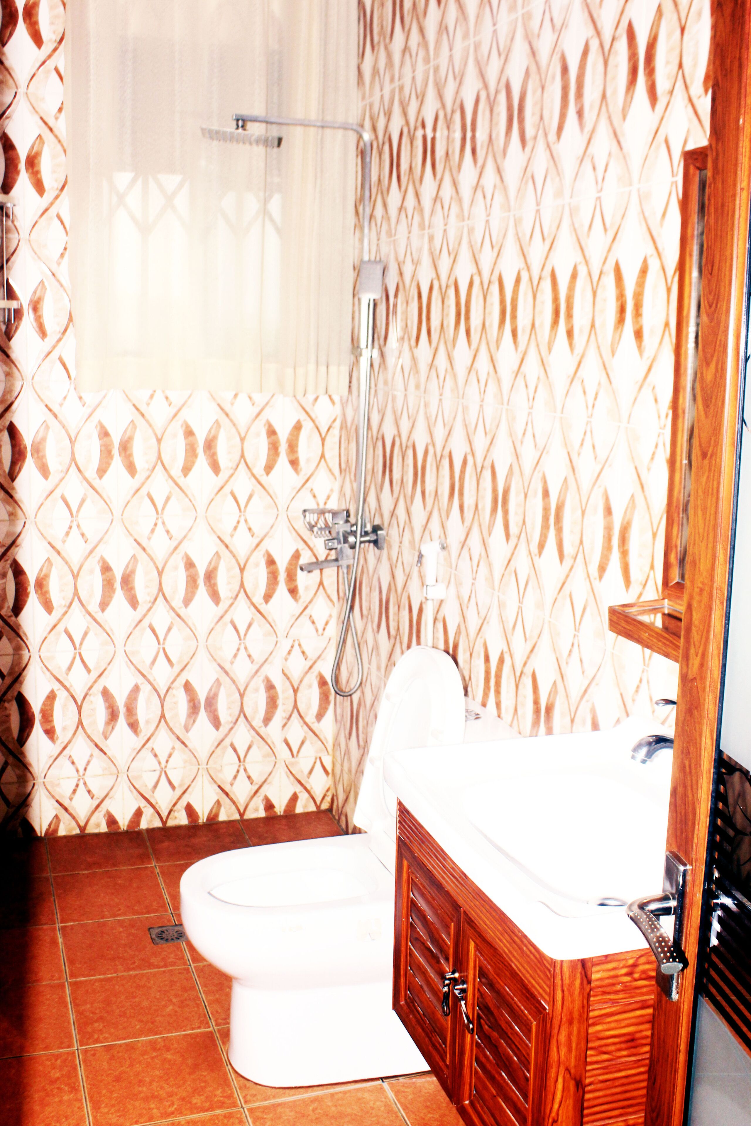 A bathroom with a white toilet, wooden vanity, and a shower with a patterned wall.