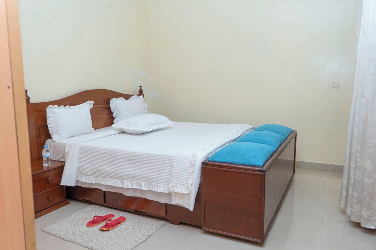 A neatly made bed with white bedding, a wooden headboard, and a blue cushion on the footboard.