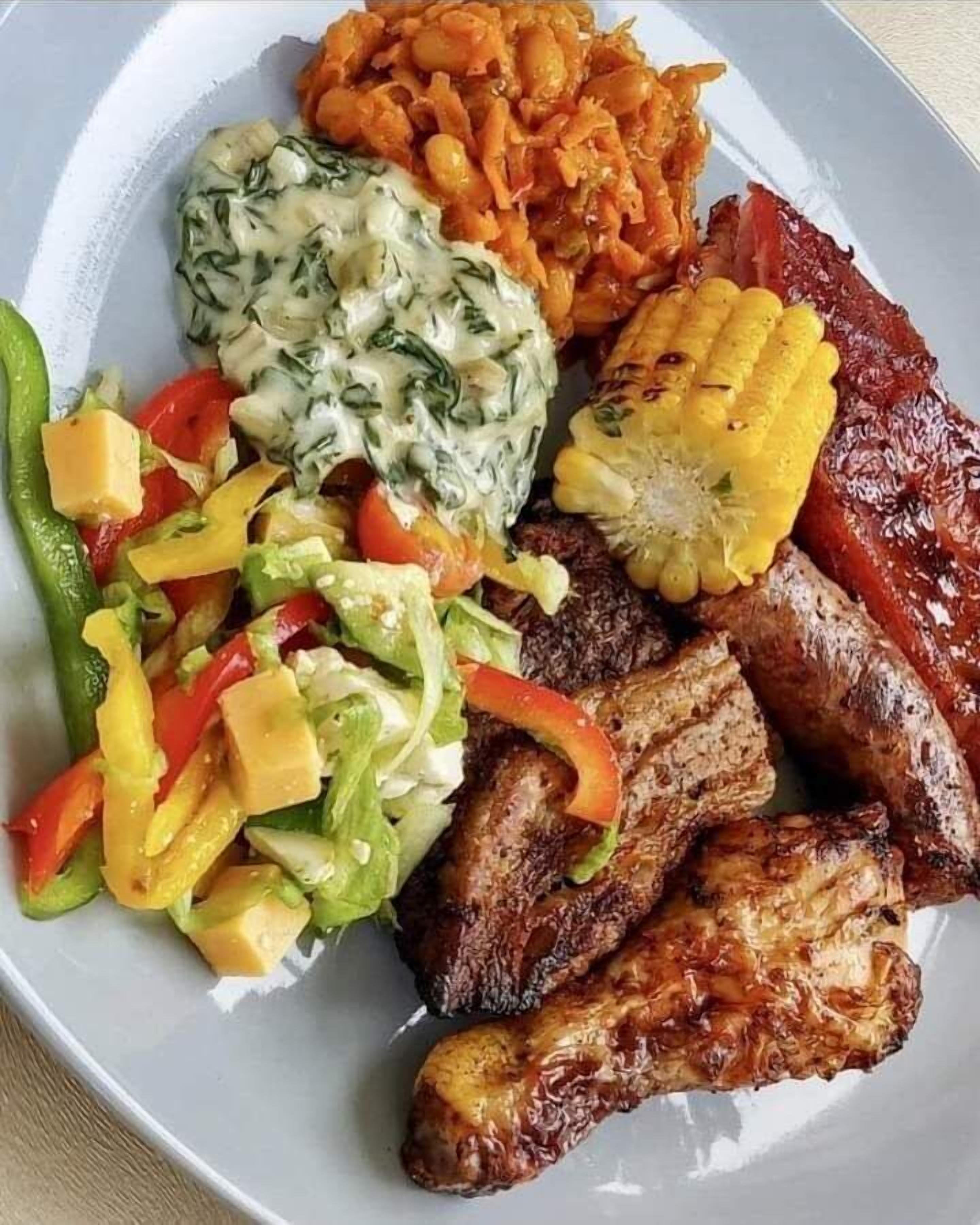 Un plato con carne a la parrilla, mazorca de maíz, ensalada y un guiso cremoso de espinacas.