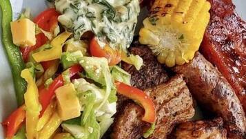 Un plato con carne a la parrilla, mazorca de maíz, ensalada y un guiso cremoso de espinacas.