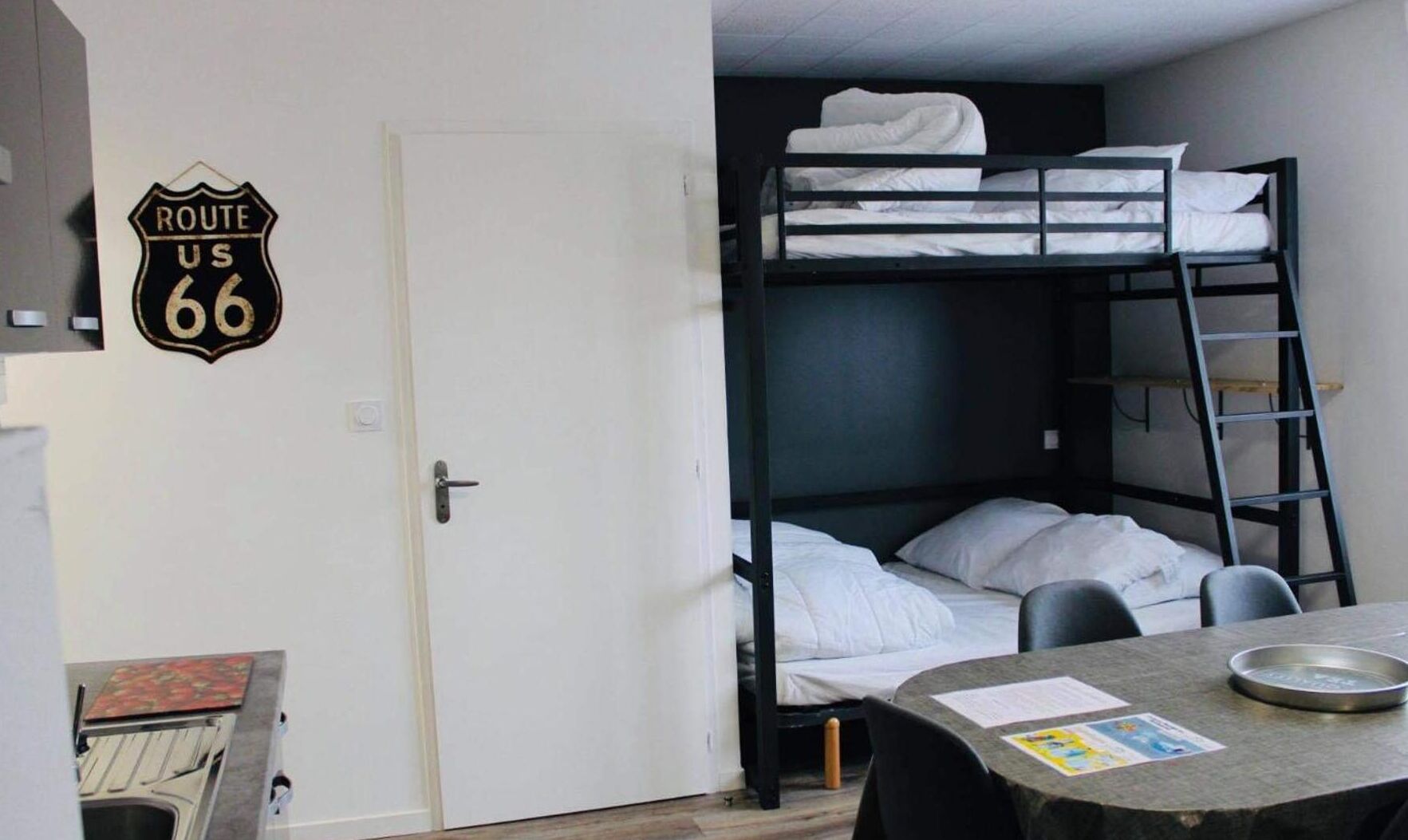 Een slaapkamer met een stapelbed, een bureau, een stoel en een deur met een 'Route US 66' bord.