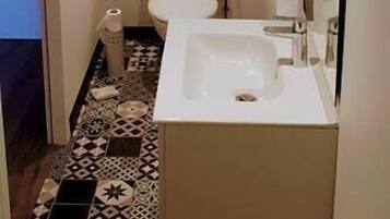 Een kleine badkamer met toilet, wastafel en spiegel. De vloer heeft een betegeld patroon.