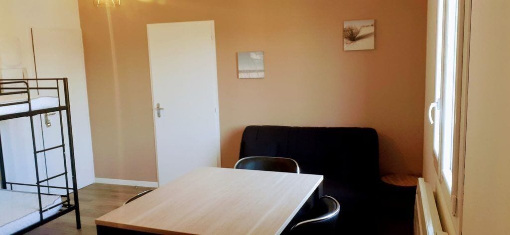 Ett rum med våningssängar, ett bord, en stol och ett fönster.