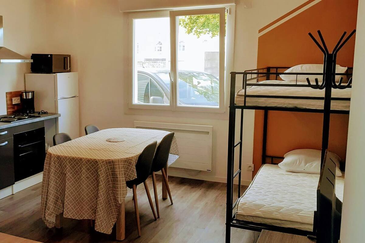Une cuisine compacte équipée d’une cuisinière, d’un évier et de placards, une table à manger avec des chaises, un lit superposé et une fenêtre donnant sur la rue.