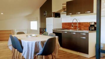A compact kitchen with a dining area, featuring a refrigerator, stove, and a coffee maker.