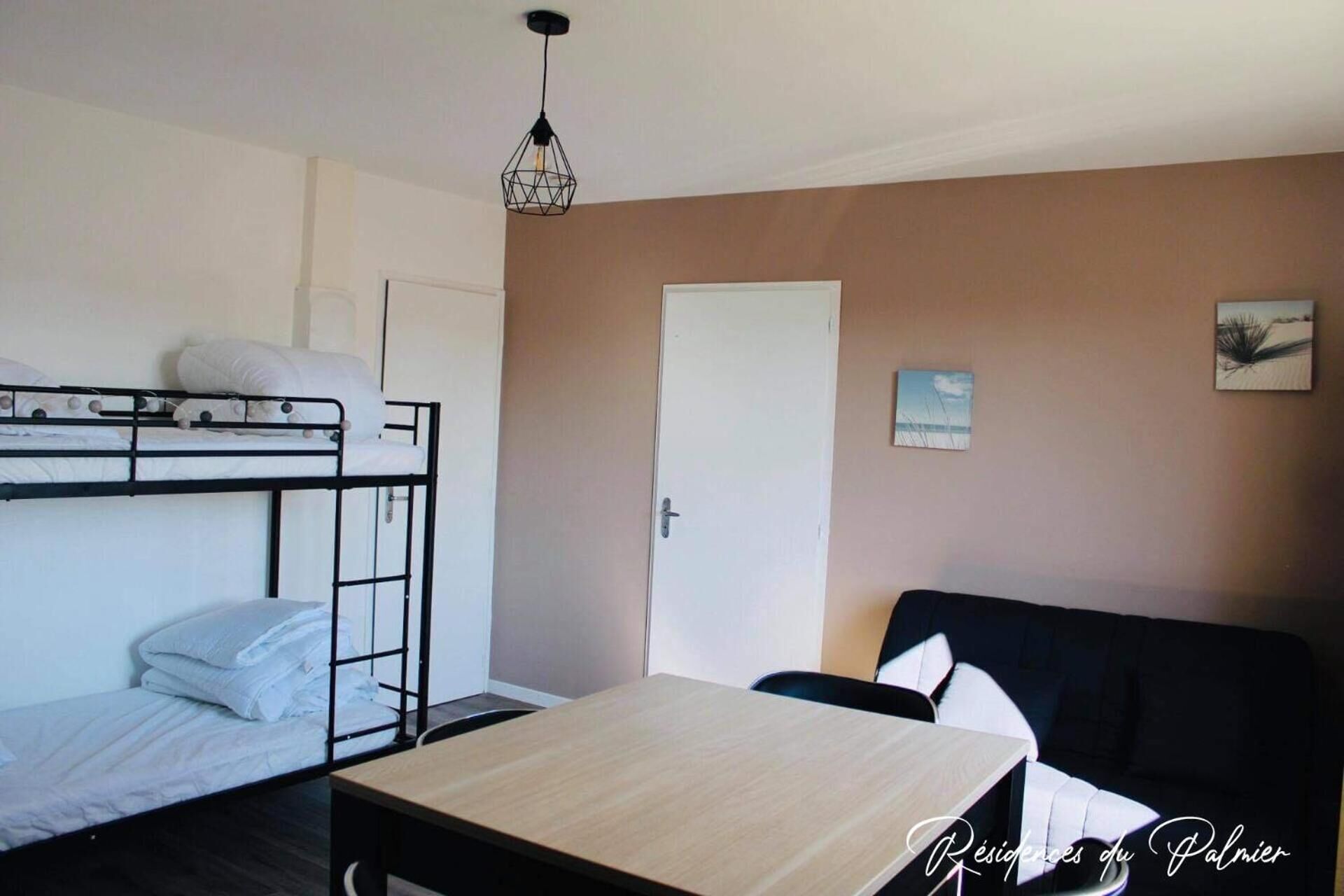 A room with bunk beds, a desk, a chair, a sofa, a door, and a wall-mounted picture.