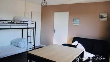 A room with bunk beds, a desk, a chair, a sofa, a door, and a wall-mounted picture.