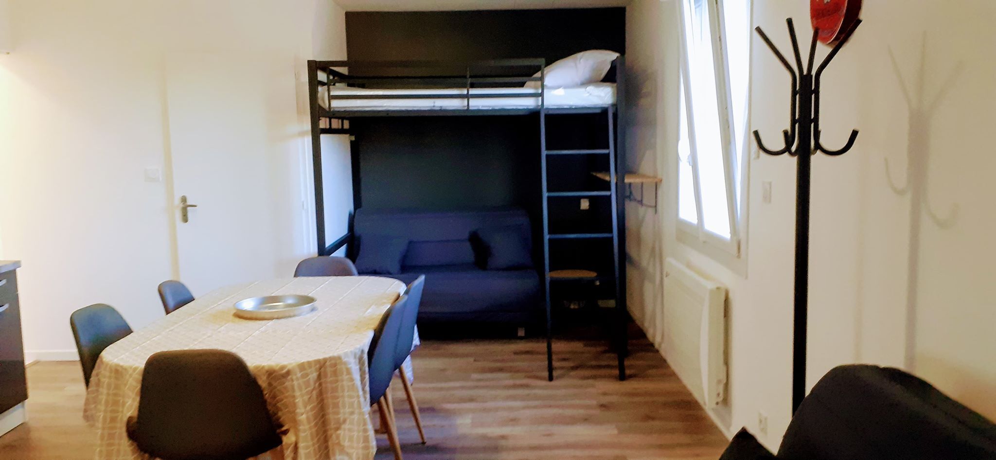 A compact room with a bunk bed, a dining table with chairs, and a coat rack.